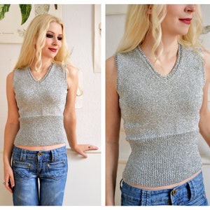 May include: A silver sleeveless top with a V-neck and a ribbed texture. The top is made of a sparkly material and has a fitted silhouette.