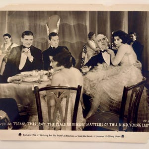 May include: A black and white vintage film still featuring a group of people in formal attire at a dinner table. The text at the bottom reads: 1188-30 "PLEASE, THIS ISN'T THE PLACE TO DISCUSS MATTERS OF THIS KIND, YOUNG LADY!" Richard Dix in "Nothing But The Truth" with Helen Kane and Louis John Bartels. A Paramount All-Talking Picture.