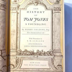 May include: A vintage book cover with an ornate frame and the title "The History of Tom Jones, A Foundling" by Henry Fielding. The cover is yellowed with age and has a decorative floral design at the bottom.