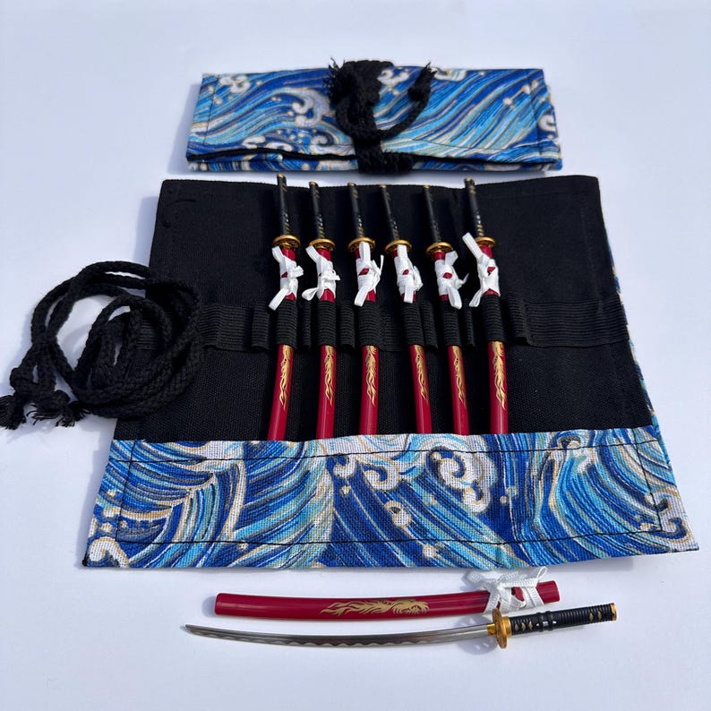 May include: A set of miniature decorative swords with red handles and gold accents, displayed in a black and blue wave-patterned case. The set includes a larger sword with a red sheath and a black handle.