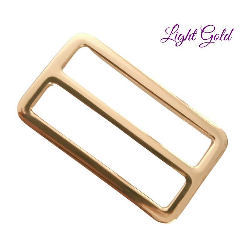K&ouml;nnte beinhalten: Ein hellgoldener rechteckiger Schiebeschnallenverschluss mit zwei parallelen &Ouml;ffnungen. Der Text "Light Gold" ist kursiv in der oberen rechten Ecke geschrieben. Die Schnalle besteht aus gl&auml;nzendem Metall.