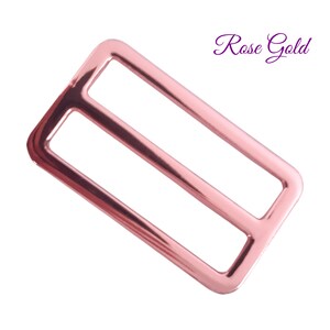 K&ouml;nnte beinhalten: Ros&eacute;goldene Metall-Schiebeschnalle mit rechteckiger Form und zwei inneren St&auml;ben. Die Schnalle hat eine gl&auml;nzende, reflektierende Oberfl&auml;che. Die Worte "Rose Gold" sind in Kursivschrift oben rechts geschrieben.