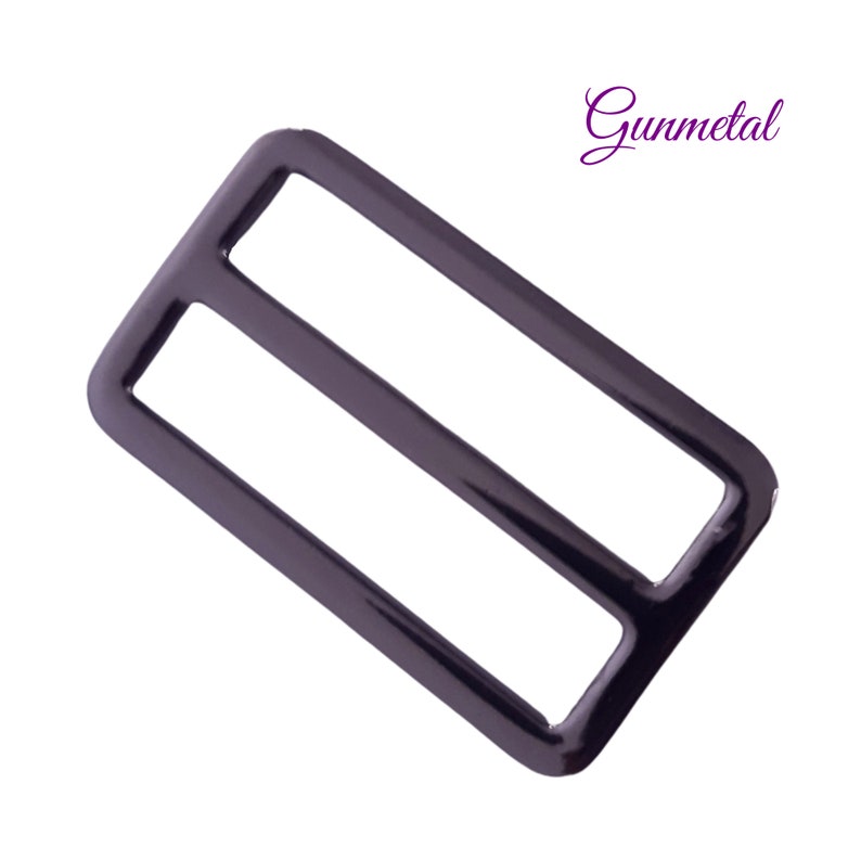 K&ouml;nnte beinhalten: Rechteckige Schiebeschnalle in Gunmetal-Farbe mit zwei parallelen St&auml;ben. Die Schnalle hat eine gl&auml;nzende Oberfl&auml;che und ist vor einem wei&szlig;en Hintergrund platziert. Das Wort "Gunmetal" ist kursiv geschrieben.