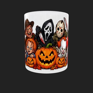May include: A white ceramic mug featuring a colourful graphic illustration of five iconic horror movie characters positioned behind three glowing orange jack-o'-lanterns with carved faces and autumn leaves at the base of the pumpkins.