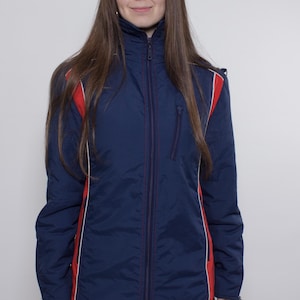 Könnte beinhalten: Marineblaue Jacke mit roten und weißen Akzenten. Die Jacke hat einen hohen Kragen und einen durchgehenden Reißverschluss. Rote Streifen verlaufen an den Seiten. Getragen mit schwarzer Kleidung und roten Leggings.