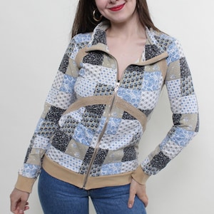 May include: A long-sleeve zip-up jacket featuring a patchwork pattern of blue, white, gray, and tan squares with various floral and paisley prints. The jacket includes a tan collar, tan cuffs, a tan hem, and tan mesh-like side panel accents.