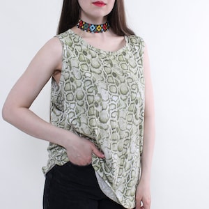 May include: A sleeveless top with a snakeskin pattern in shades of green and white. The model is wearing a colourful beaded choker and black jeans. The top has a scoop neckline.