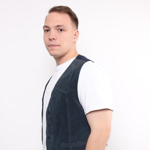 Könnte beinhalten: Ein Mann trägt eine dunkelblaue Wildlederweste über einem weißen T-Shirt und einer schwarzen Hose.