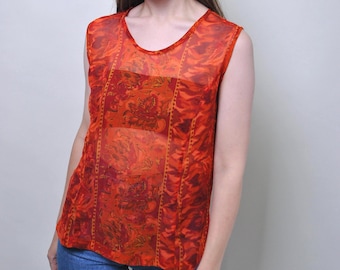 Op de afbeelding: Een mouwloze top in een levendige oranje en rode bloemenprint met een doorschijnende, lichtgewicht stofconstructie. Het kledingstuk heeft een ronde halslijn en een gestructureerd paneelontwerp met verticale details, gecombineerd met een blauwe spijkerbroek.