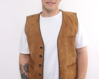 May include: A brown suede vest with a white t-shirt underneath. The vest has a dark brown trim and five buttons down the front.