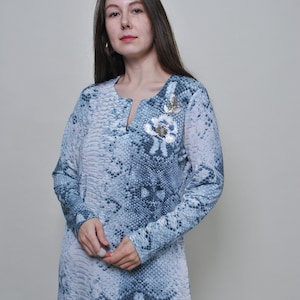 Peut inclure: Un chemisier à manches longues, à motif bleu et blanc, avec un imprimé peau de serpent et un embellissement floral sur la poitrine.