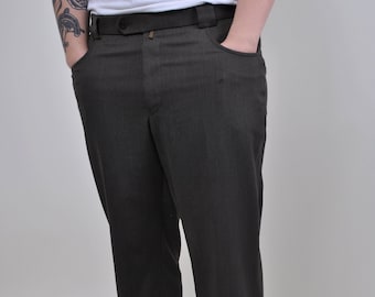 May include: A pair of dark gray pinstripe pants with a button fly and belt loops. The pants are worn by a person with a tattoo on their arm. The person is wearing black sneakers.