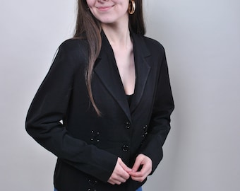 Puede incluir: Una mujer con un blazer negro con costuras decorativas y pantalones vaqueros azules. Está sonriendo y mirando hacia un lado.