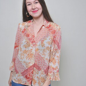 May include: A long-sleeved button-down shirt with a floral print in shades of orange, red, and white. The shirt has a relaxed fit and a collar.