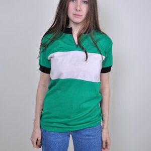 Op de afbeelding: Een groen-wit gestreept shirt met korte mouwen en een zwarte rits. Het shirt heeft een witte horizontale streep over de borst.