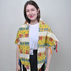 May include: A yellow, white, and green plaid shawl with colorful tassels. The shawl is made of a patchwork of different fabrics and has a fringed edge.