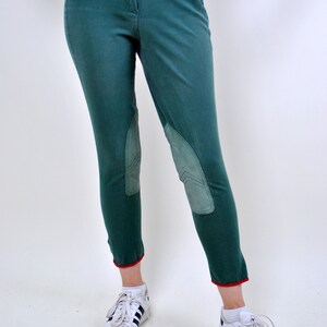 May include: Green riding pants with knee patches and red trim at the bottom. The pants are worn with white sneakers with black stripes.