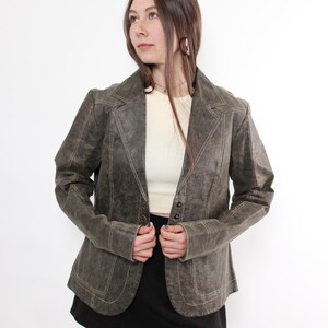 Puede incluir: Blazer verde oliva de estilo vintage con cuello de solapa y cierre de tres botones. La chaqueta presenta costuras visibles y se combina con una falda negra y medias rojas. Una prenda de vestir exterior cl&aacute;sica.