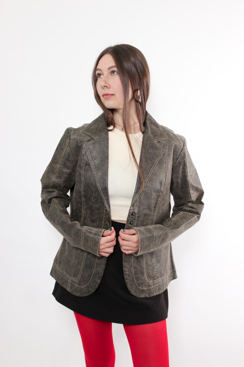 Puede incluir: Blazer verde oliva de estilo vintage con cuello de solapa y cierre de tres botones. La chaqueta presenta costuras visibles y se combina con una falda negra y medias rojas. Una prenda de vestir exterior cl&aacute;sica.