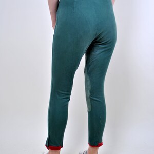 May include: A pair of dark green riding pants with red trim at the bottom of the legs. The pants have a knee patch on each leg.