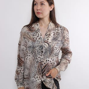 May include: A button-down shirt with a unique animal print design. The shirt features a mix of zebra stripes and leopard spots in shades of brown, beige, and black. The long-sleeved shirt has a classic collar and is made of a lightweight fabric.