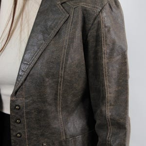 Puede incluir: Blazer de cuero marr&oacute;n con solapa de muesca y cierre de tres botones. El blazer tiene costuras visibles y un acabado texturizado. La chaqueta es de estilo vintage.