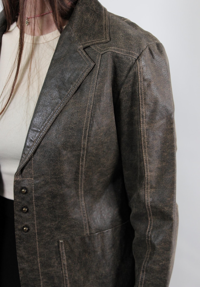 Puede incluir: Blazer de cuero marr&oacute;n con solapa de muesca y cierre de tres botones. El blazer tiene costuras visibles y un acabado texturizado. La chaqueta es de estilo vintage.