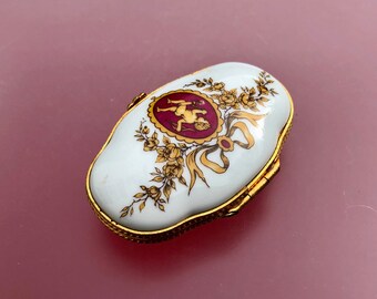 Vintage Limoges porcelain trinket box decorated with a cherub and finished in red and gold