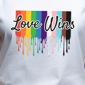 May include: White t-shirt with a rainbow dripping paint design and the text "Love Wins" in black.