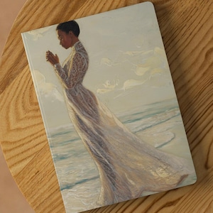 May include: A woman in a white flowing dress stands on a beach with her head bowed in prayer. The sky is a soft blue with white clouds. The beach is sandy with blue water.