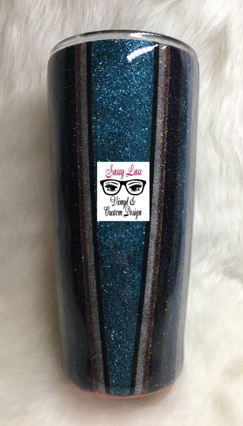 Op de afbeelding: Een turquoise, zwart, zilver en roze glitterbeker met verticale strepen. De beker heeft een doorzichtig deksel en een roze basis. De beker heeft een logo met de tekst "Sassy Lass Vinyl & Custom Design" met een bril en wimpers.