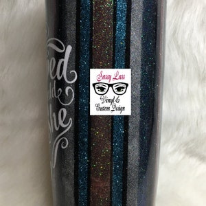 Op de afbeelding: Een zwarte en zilveren glitterbeker met een ontwerp van teal, bruin en zwarte strepen. De beker heeft een wit vinylontwerp met de tekst "Loved and She" en een logo met de tekst "Sassy Lass Vinyl & Custom Design".