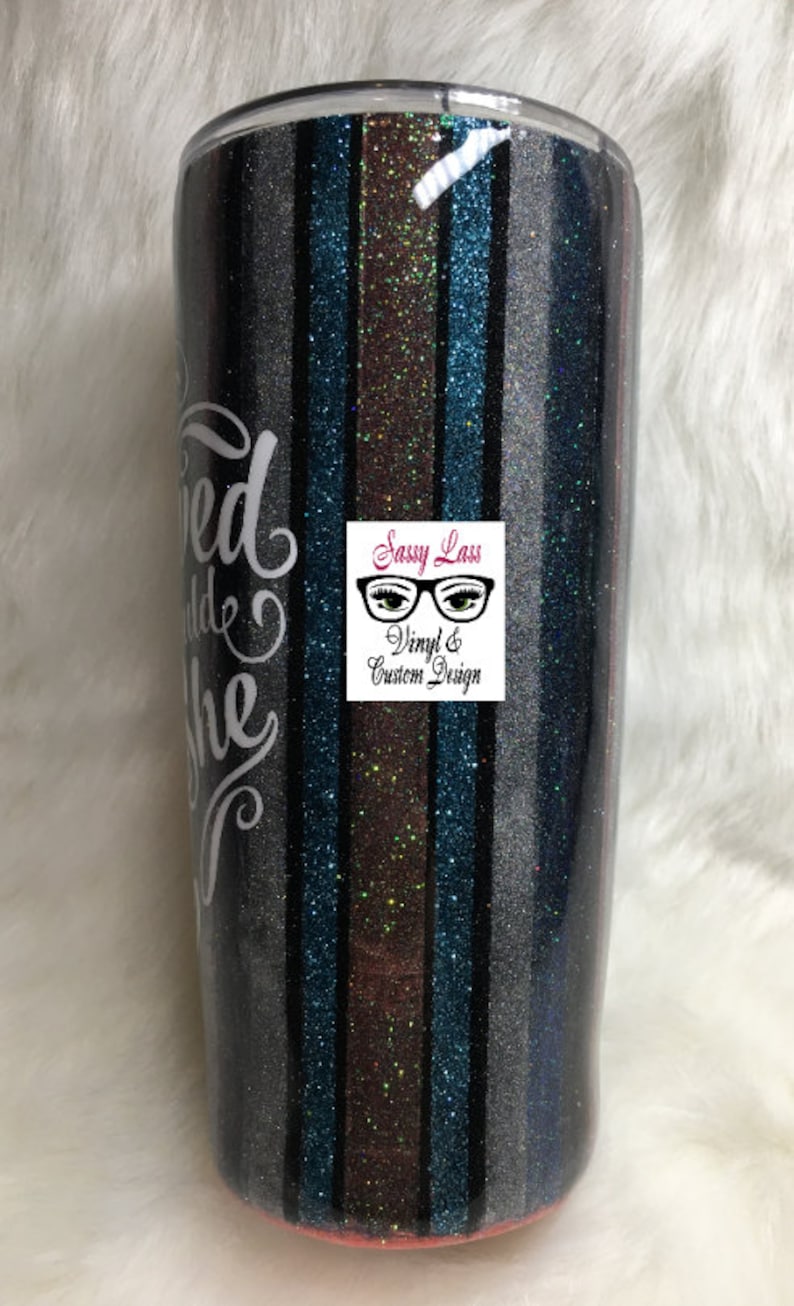 Op de afbeelding: Een zwarte en zilveren glitterbeker met een ontwerp van teal, bruin en zwarte strepen. De beker heeft een wit vinylontwerp met de tekst "Loved and She" en een logo met de tekst "Sassy Lass Vinyl & Custom Design".