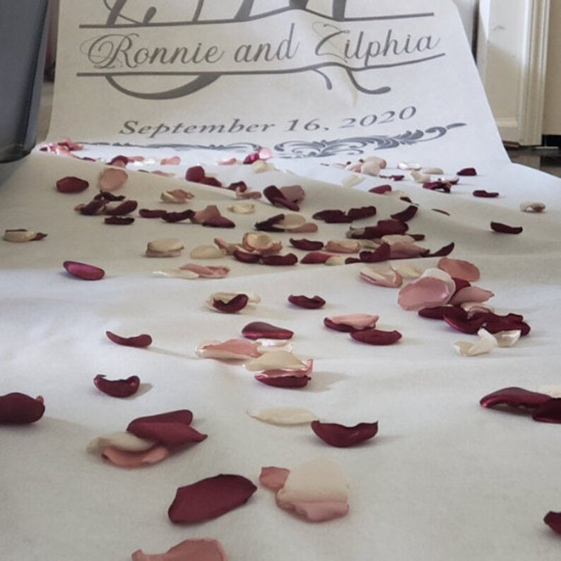 May include: A white aisle runner with the text "Ronnie and Zilphia" and "September 16, 2020" is covered in scattered rose petals.