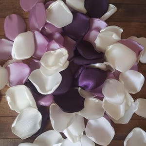 Könnte beinhalten: Ein Haufen Seidenrosenblätter in Weiß, Lavendel und Lila. Die Blütenblätter sind in einem zufälligen Muster angeordnet, wobei sich einige überlappen.