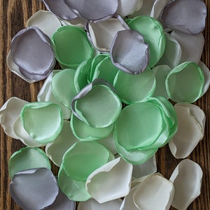 May include: A pile of satin flower petals in shades of white, green, and gray. The petals are arranged in a random pattern on a wooden surface.