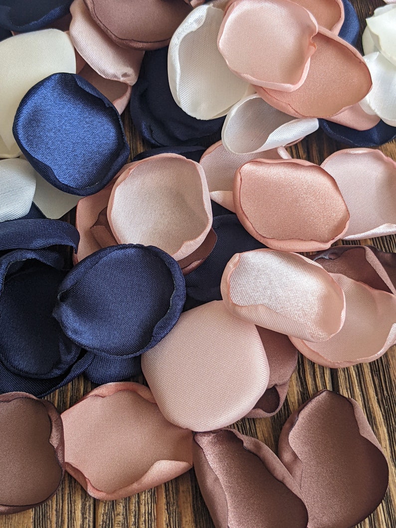 May include: Assortment of fabric flower petals in navy blue, blush pink, ivory white, and brown. The petals are made of satin and are perfect for wedding decorations or crafting projects.