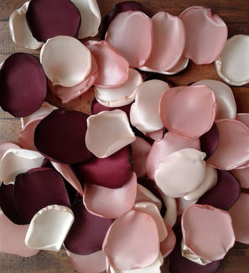 May include: A collection of burgundy, blush pink, and ivory satin rose petals. The petals are arranged in a random pattern and are perfect for wedding decorations or other special events.