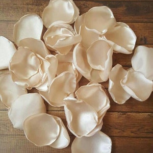 May include: A pile of ivory satin rose petals. The petals are soft and delicate, perfect for wedding decorations or special events.