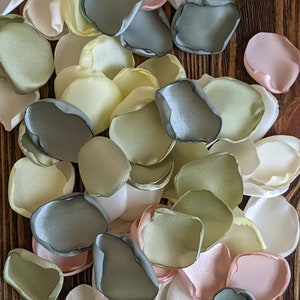 May include: Assortment of silk flower petals in shades of green, white, and pink. The petals are scattered on a wooden surface.