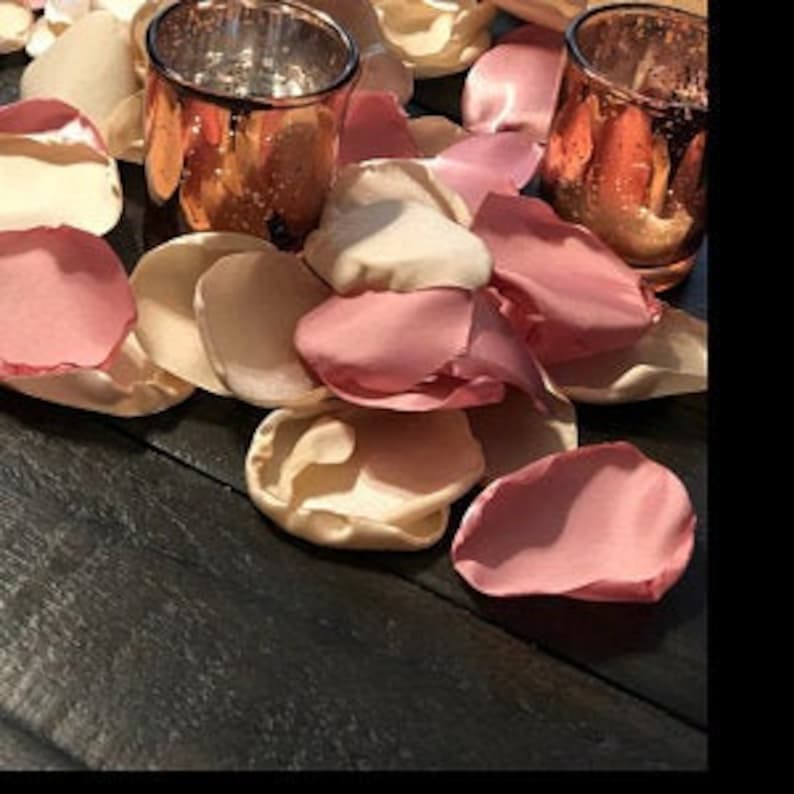 May include: A pile of rose petals in pink, cream, and ivory colors on a dark wood surface. Two copper-colored glass candle holders are in the background.