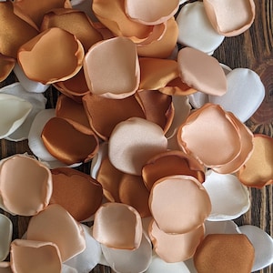 Könnte beinhalten: Ein Haufen Seidenrosenblätter in Elfenbein-, Pfirsich- und Kupfertönen. Die Blütenblätter sind auf einer Holzoberfläche verstreut.