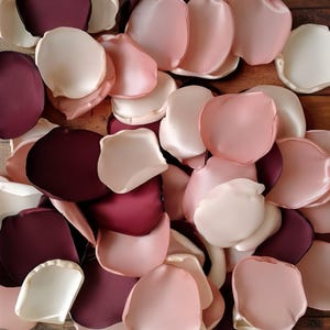 May include: A pile of silk rose petals in shades of burgundy, blush pink, and ivory. The petals are arranged in a random pattern, creating a romantic and elegant look.