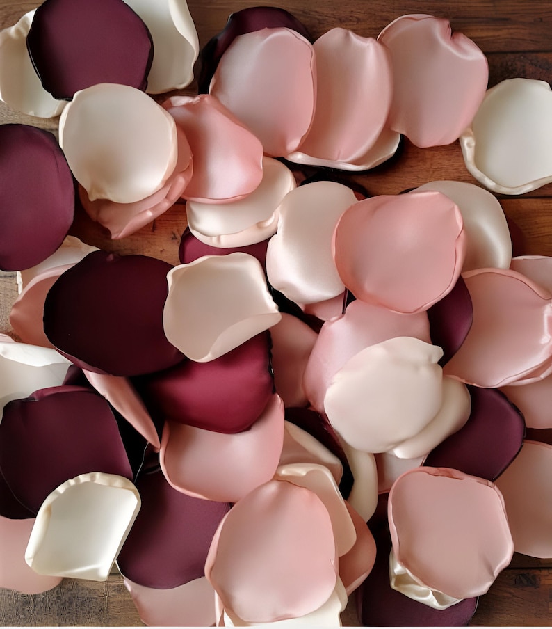 May include: A pile of silk rose petals in shades of burgundy, blush pink, and ivory. The petals are arranged in a random pattern, creating a romantic and elegant look.