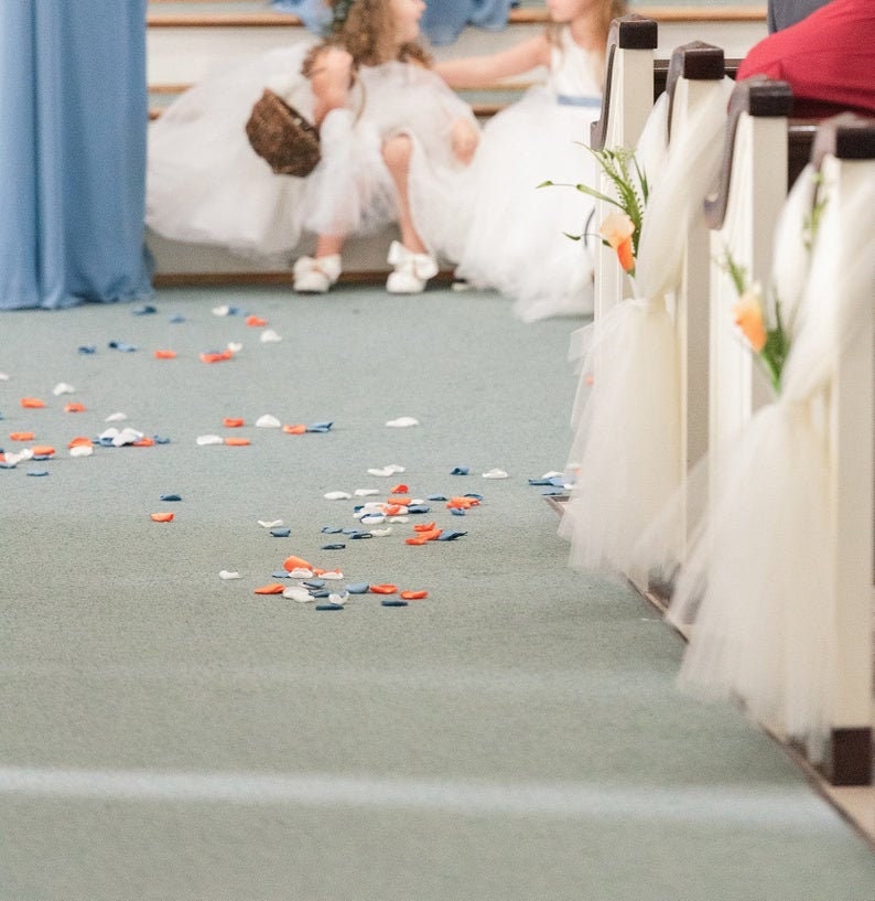 May include: A wedding aisle decorated with white tulle and peach flowers. Scattered on the floor are blue, white, and orange flower petals.