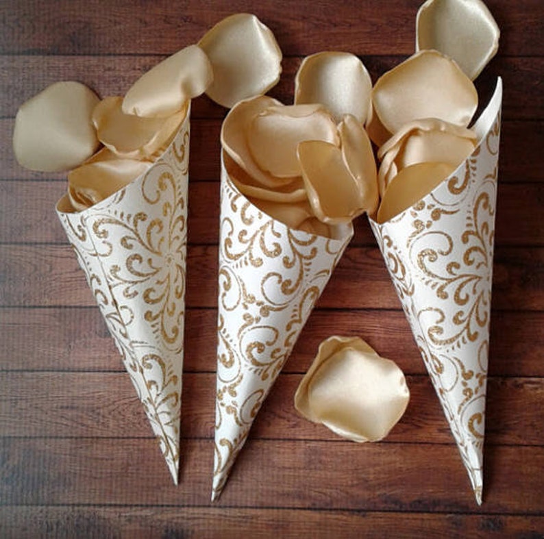 May include: Three white paper cones filled with ivory satin rose petals. The cones have a gold glitter pattern.
