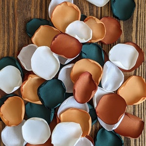 Può includere: Un mucchio di petali di fiori di stoffa di colore bianco, arancione, marrone e verde scuro. I petali sono disposti in modo casuale su una superficie di legno.