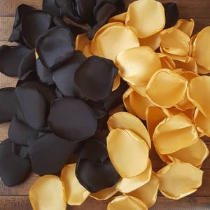 May include: Black and gold satin rose petals. The petals are arranged in a pile, with the black petals on the bottom and the gold petals on top.