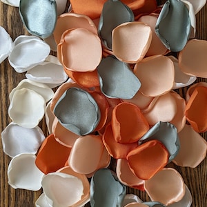 May include: A collection of silk flower petals in shades of peach, white, and gray. The petals are arranged on a wooden surface.