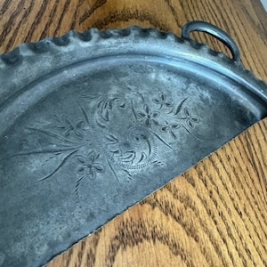 May include: A silver, scalloped, half-circle serving tray with a floral design. The tray has a handle on the right side.